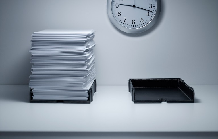 A tall stack of white paper in a black tray beside a second black tray that is empty on a white background with a clock.