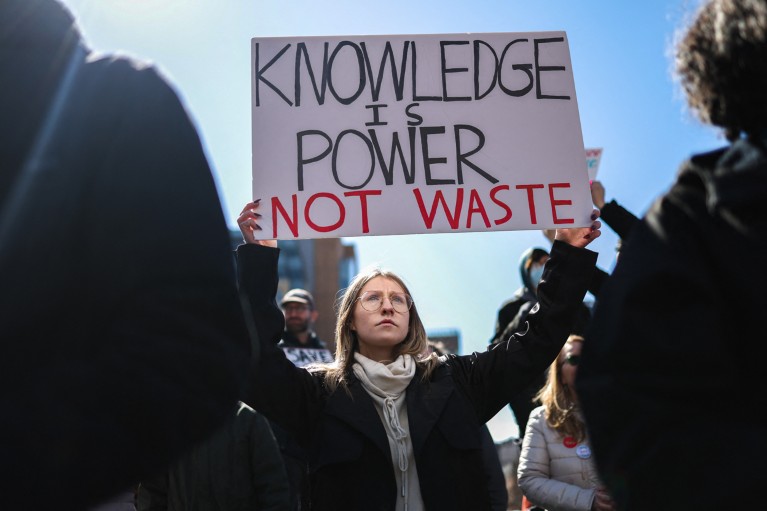 A protester holds up a white sign reading: "knowledge is power not waste"