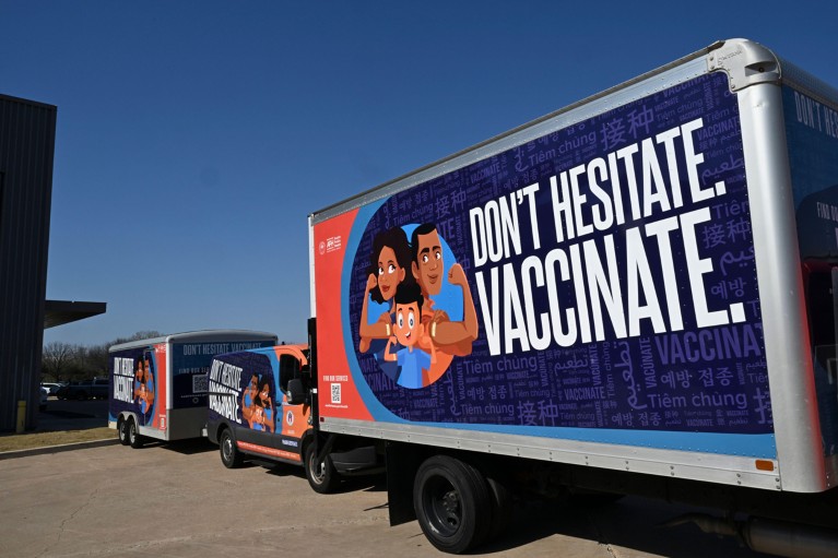 Three blue trucks are lined up with signs that read: "Don't hesitate. Vaccinate."