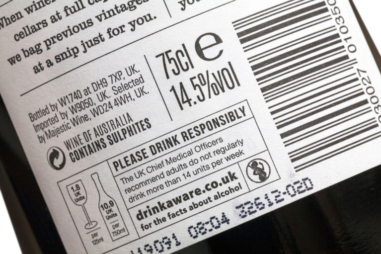 Primo piano di un'etichetta bianca su una bottiglia di vino rosso che mostra la percentuale di alcol, una casella "si prega di bere responsabilmente" e un simbolo di avvertenza sul consumo di alcol durante la gravidanza