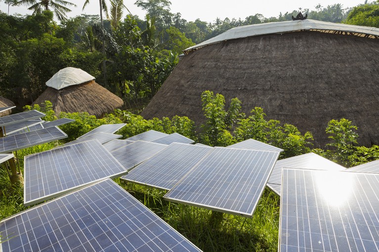 Several square solar panels among thatched roof buildings in Ubud District, Indonesia.