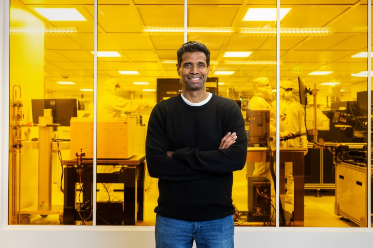 Chetan Nayak posing for a portrait by a window a clean room lab, in which everything is washed in yellow light