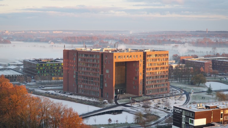 A large, red brick, modern university building at Wageningen University Campus, with mist in the distance and snow on the surrounding grounds