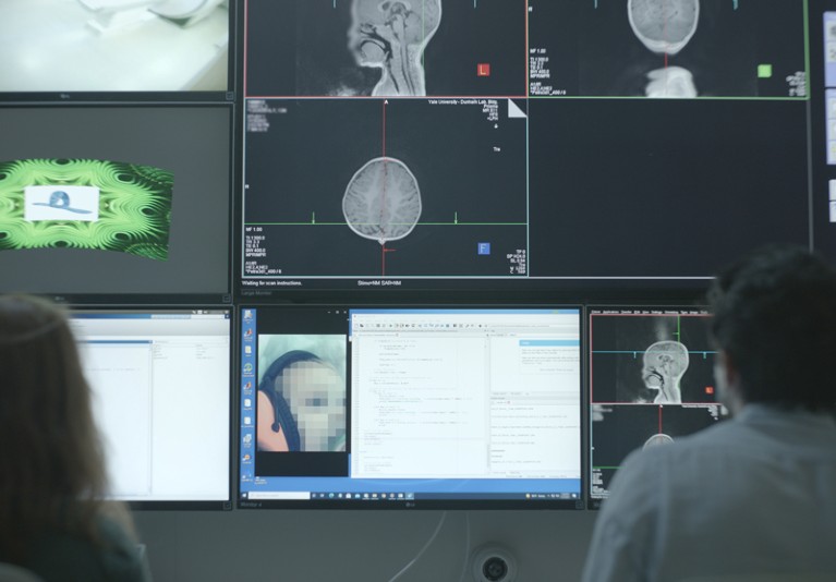 Two researchers looking at a bank of monitors displaying MRI scans of infants heads and brains