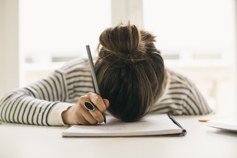 Woman writing on notepad resting her head face down on page.