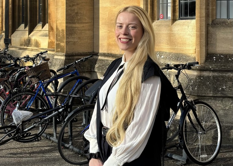A woman with blonde hair stands in a graduation gown