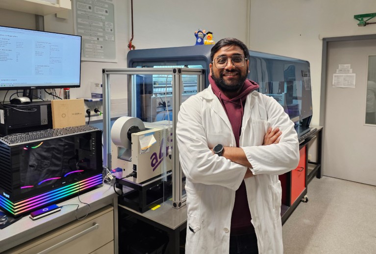 Manan Shah standing in front of a high throughput pipetting robot in a university lab.