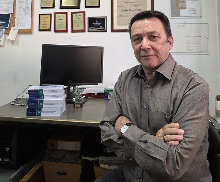 Ratko Magjarević sits in front of his desk with a computer and and books about Bioengineering.The wall displays many frames awards and accolades.