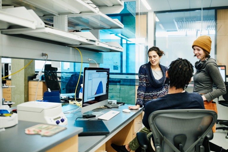 Three people smiling while talking around a computer in a lab