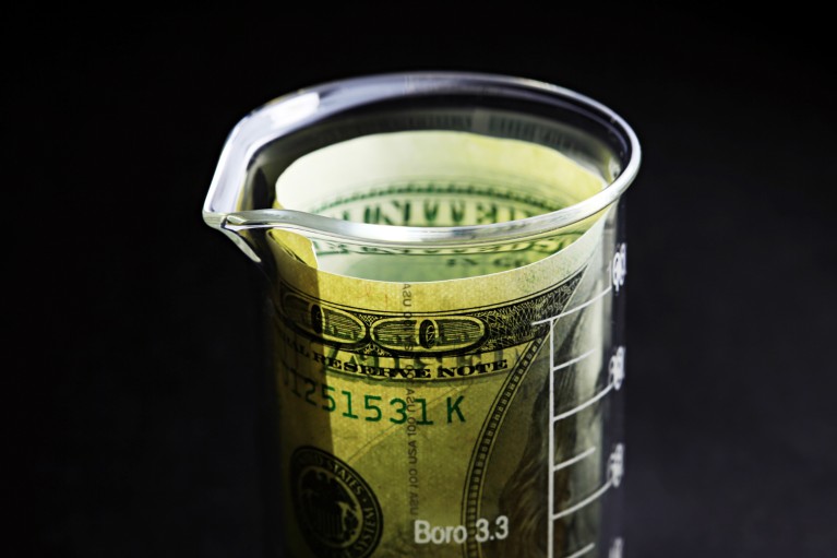 A roll of US dollars inside a small glass lab beaker on a black background