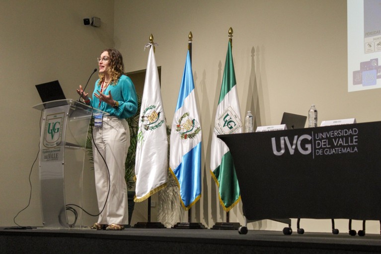Luz Cumba Garcia speaking on a stage behind a podium with three flags behind her
