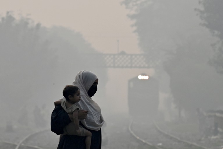 Woman wearing a headscarf carries a young boy against a backdrop of thick smog.