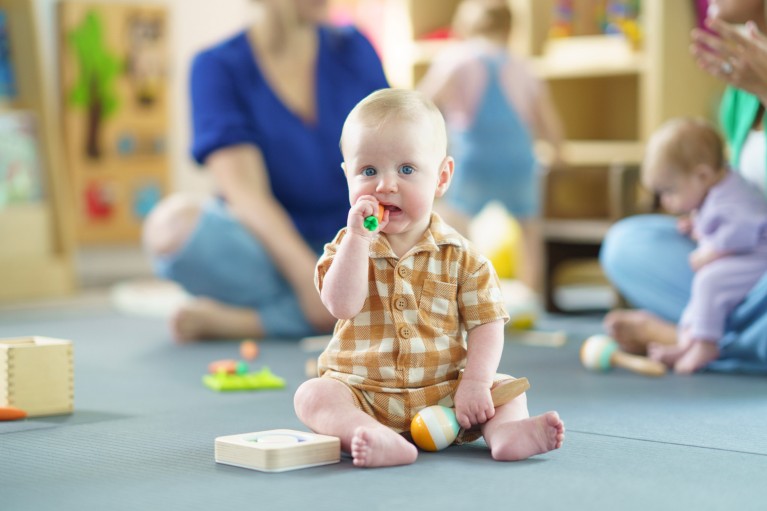 Shallow focus photograph of a young blonde haired and blue eyed baby sitting playing with toys at daycare
