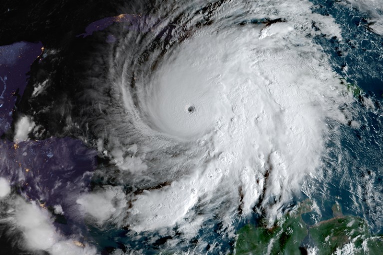 A satellite view of a huge swirling white hurricane cloud sitting over an ocean, with some islands just visible.