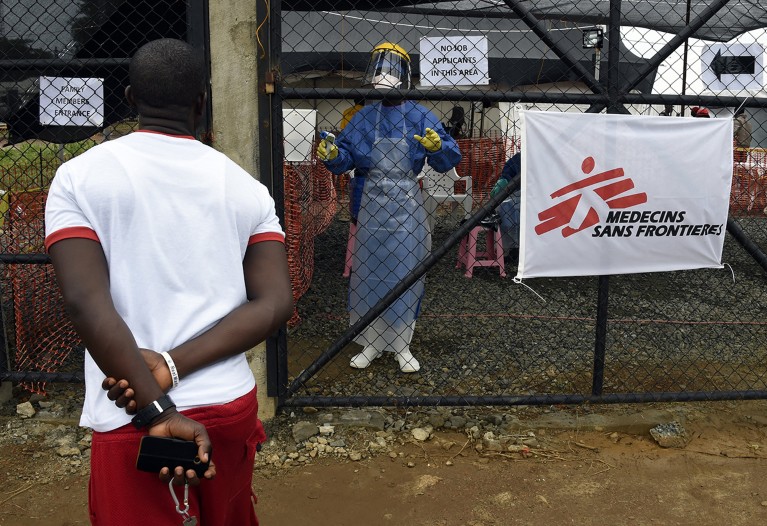 A man speaks with a health worker dressed in protective clothing beyond a security fence at the Medecin sans Frontiere medical centre.