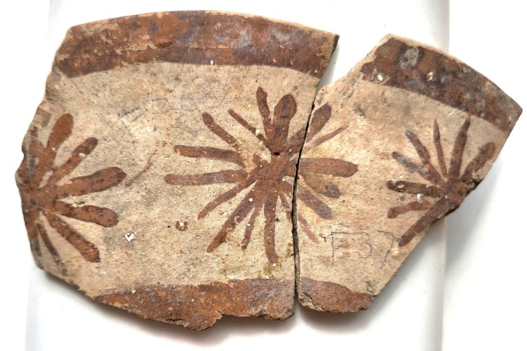 Close-up of a broken painted Halafian pottery shard with three flowers on it on a white background