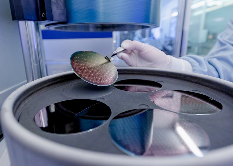 Close-up of a gloved hand holding a colourful circular object above a circular container in a cleanroom.