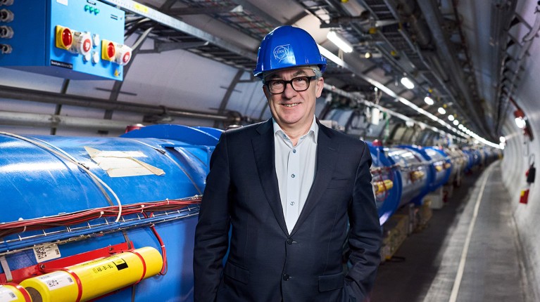 Portrait of Prof. Mark Thomson posing in the LHC tunnel wearing a blue hard hat.