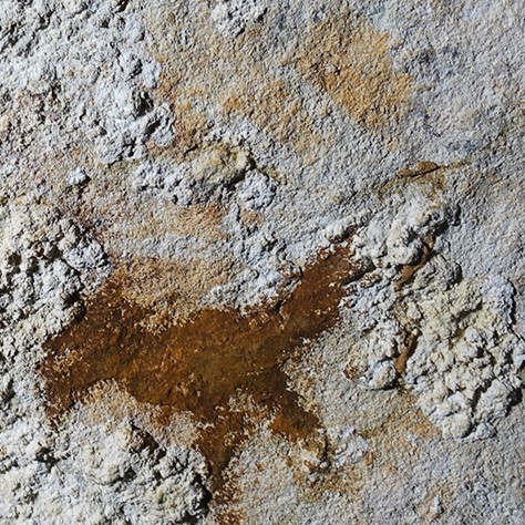 Close up view of a stencilled outline of a hand on a cave wall.