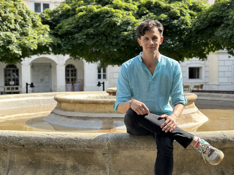 Rafael Prieto-Curiel sits on the edge of a stone fountain in a courtyard, with trees in the background