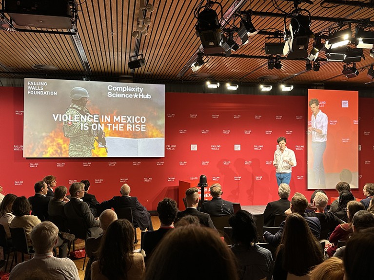 Rafael Prieto-Curiel stands on stage giving a presentation in front of an audience