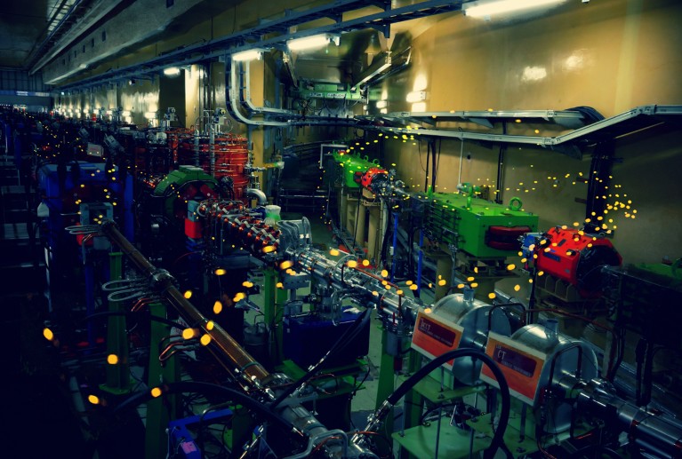 A composite image of a particle accelerator and a long-exposure of fireflies flying creating a wave of dots of lights moving around the accelerator instrument