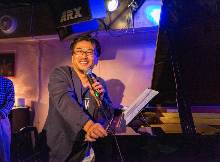 Hiroto Nagai sat at a piano while speaking during a live concert.