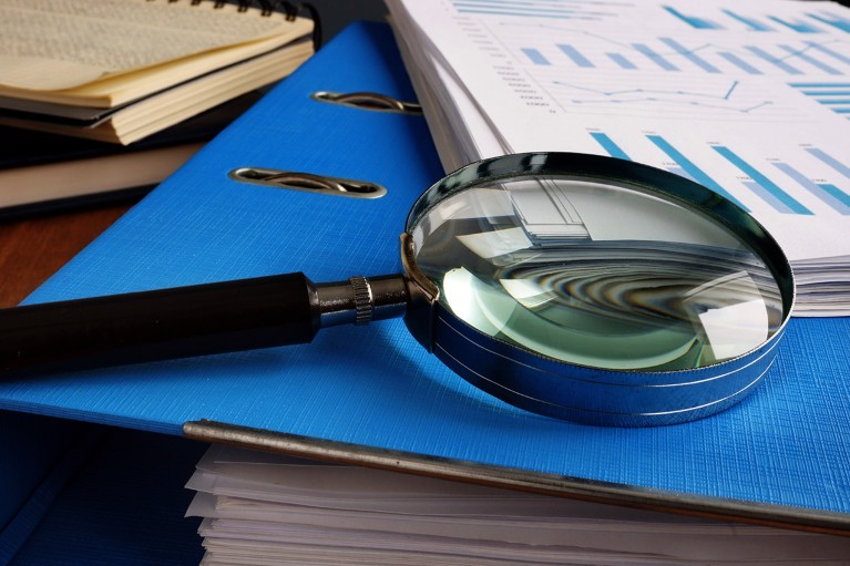 Поглед изблиза на лупу која лежи на фасцикли са гомилама папирних докумената.