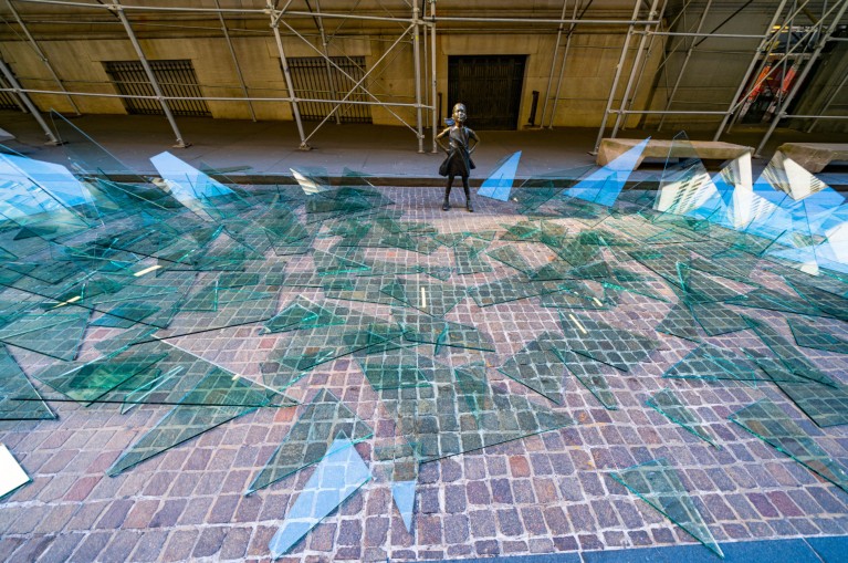 Art installation for International Women's Day showing a statue of a girl surrounded by broken shards of glass on the ground.