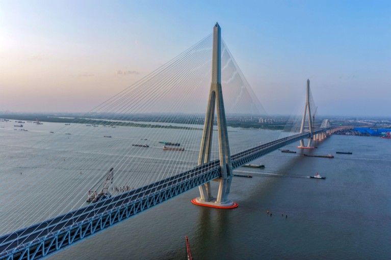 An aerial view of the cable-stayed Changtai Yangtze River Bridge with many ships passing beneath it.