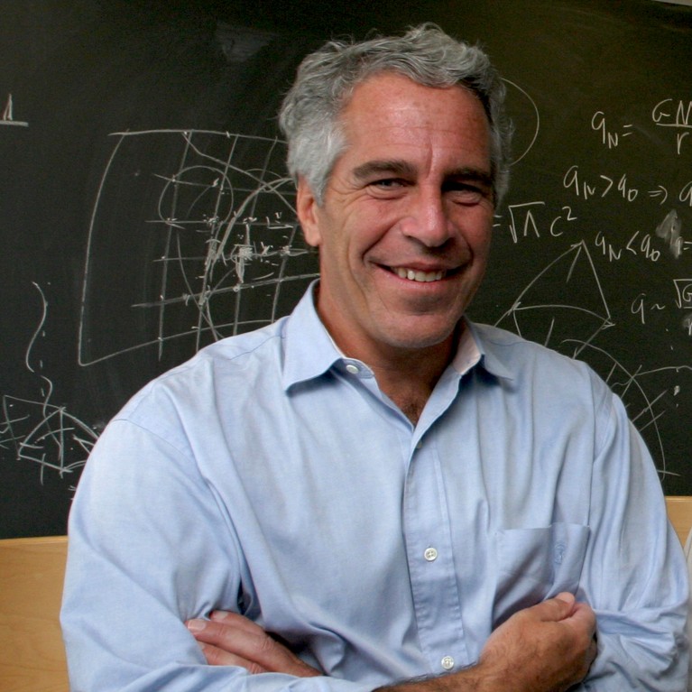 Jeffrey Epstein with his arms folded and smiling in front of a chalkboard in a classroom in 2004.