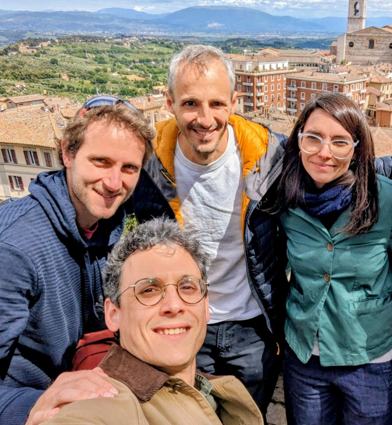 Four people taking a selfie in front of a view of a town and hills.
