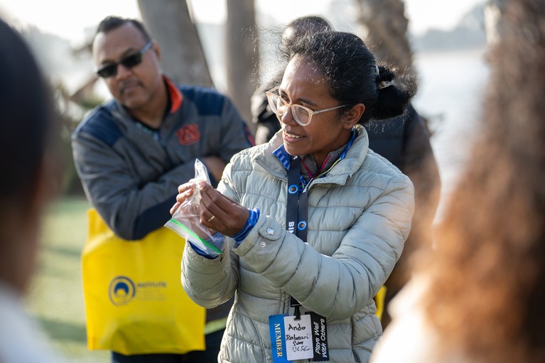 Ando Rabearisoa is in the center of a gathering of other researchers outside, examining a specimen in a plastic bag.