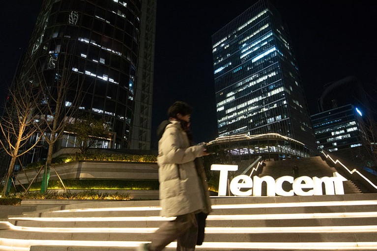 Person walking past Tencent illuminated logo at night in Shanghai