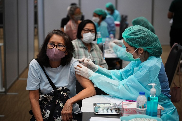 Health workers in PPE administer the COVID-19 vaccine at multiple tables to people in masks at a mass vaccination site.