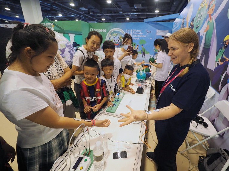 People at a science fair at a table with an instructor for an experiment involving electrical currents.