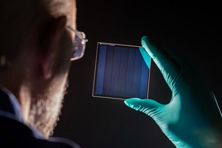 A researcher holds a piece of the laser treated glass in a gloved hand.