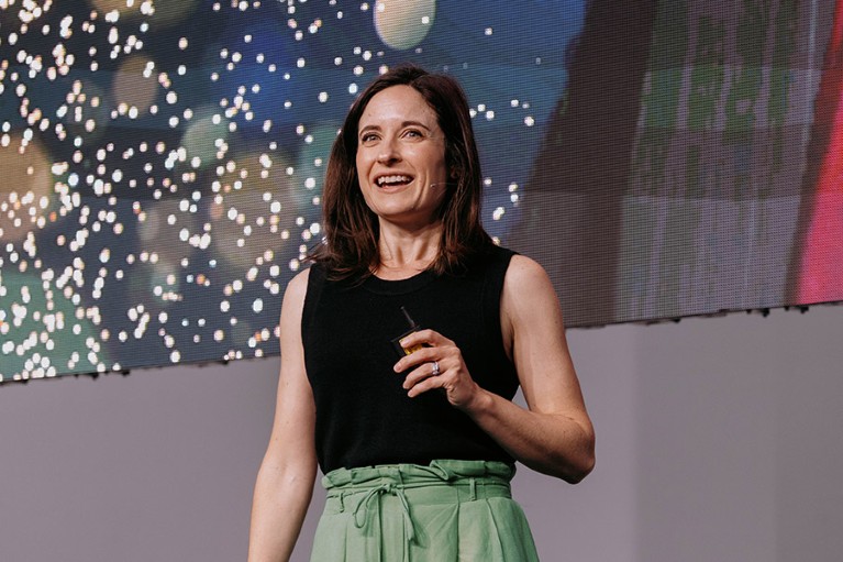White woman with dark hair smiling in front of a lit up projection screen.