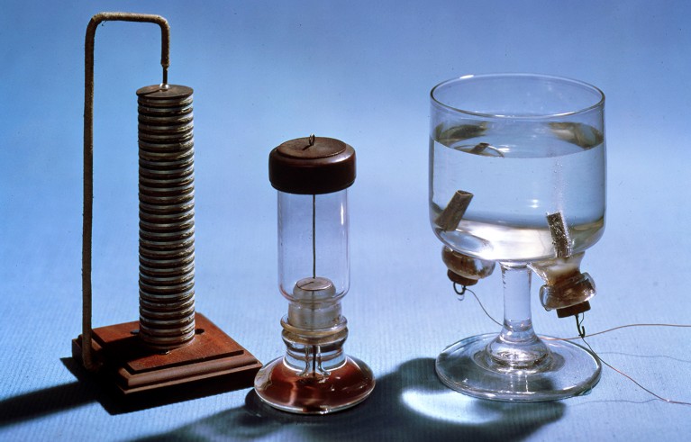 Лабораторијска опрема викторијанског изгледа, укључујући волтаичну гомилу и теглу воде са електродама у њој.