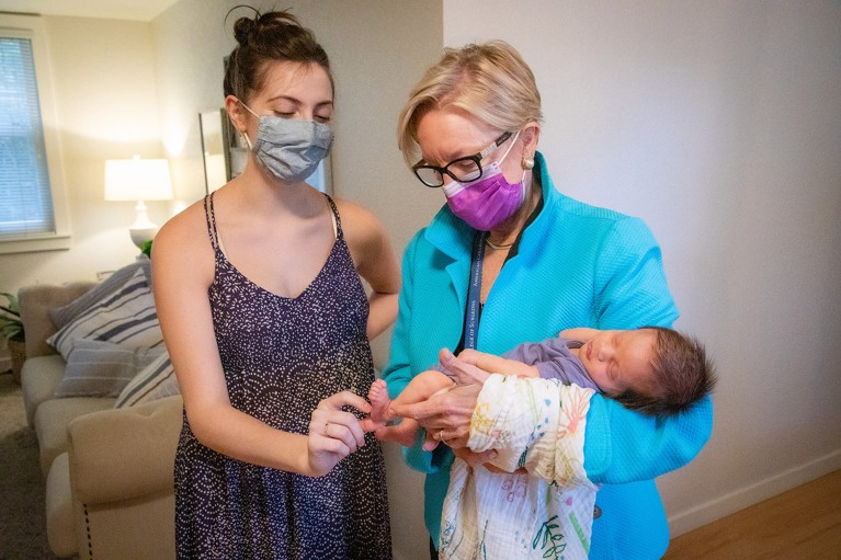 Two women wearing face masks hold a tiny baby.