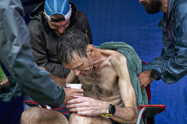 Close-up of an exhausted runner seated, drinking water and being tended to.
