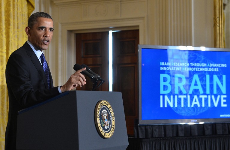 Barack Obama speaks at a podium next to a screen reading 'BRAIN Initiative'.