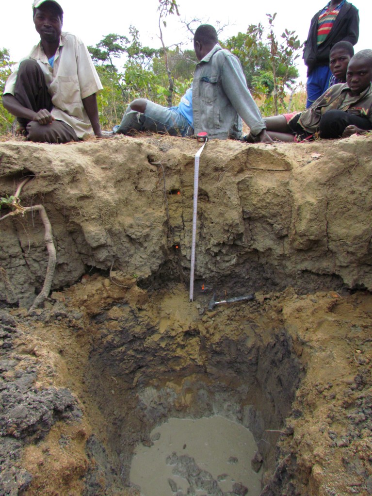 A deep pit showing water at the bottom with tired looking men resting at the top.
