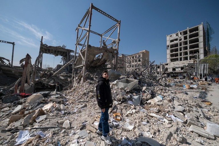 A boy standing in the rubble of bombed buildings.