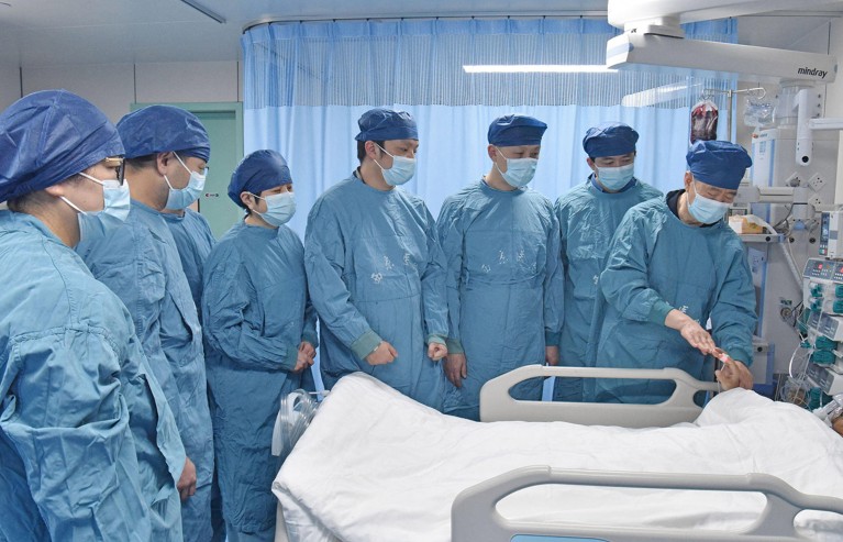 A large medical team in blue scrubs checks the condition of a patient after surgery.