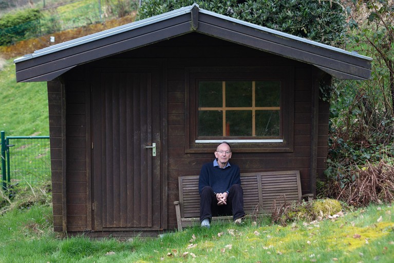 Gerd Faltings poses for a portrait sat on a wooden bench outside a shed.