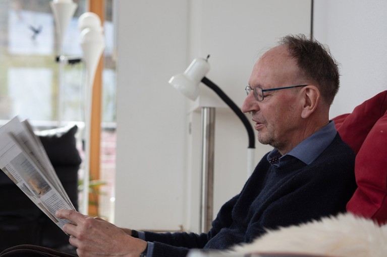 Portrait of Gerd Faltings sat of a sofa while he reads a newspaper.
