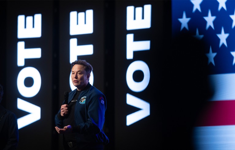Elon Musk speaks during a town hall meeting at the KI Convention Center. Flag and sign vote on the stage's background.