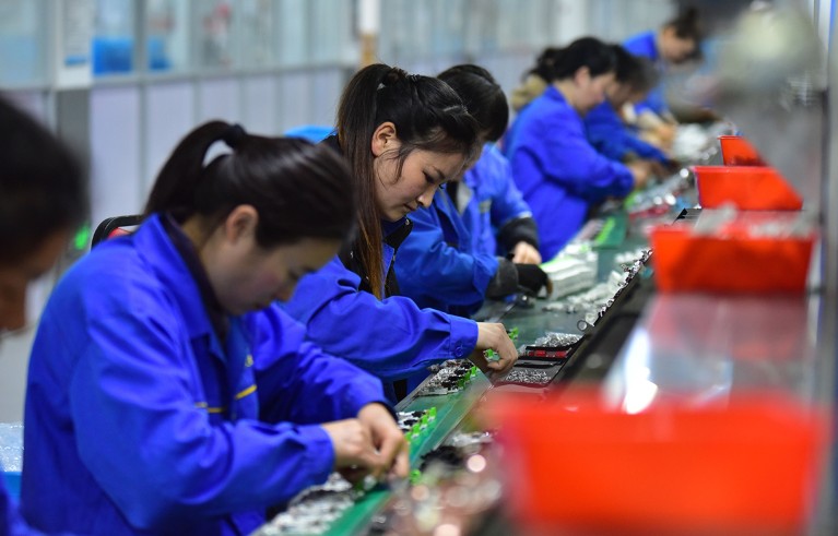 Female employees with dark hair and blue lab coats work on circuit breaker production line at Anhui, China.