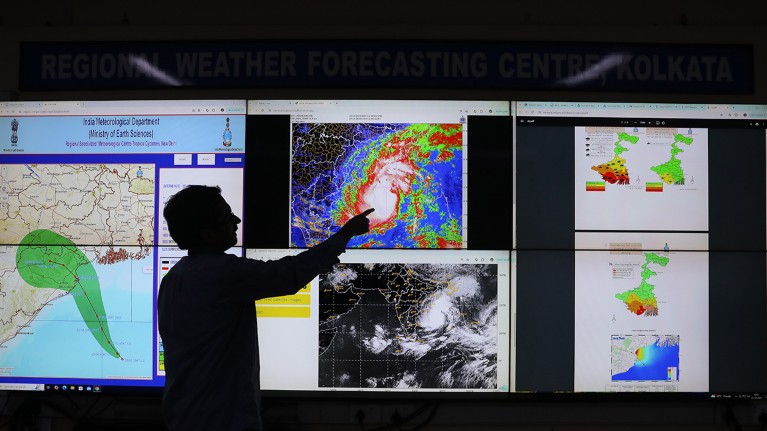 A backlit scientist at the India Meteorological Department points to a section of a monitor showing Cyclone Dana.